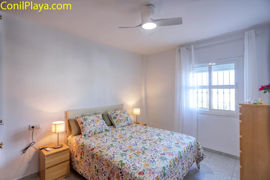 Dormitorio principal con cama doble, ventilador de techo y ventana amplia desde dónde se vé el mar