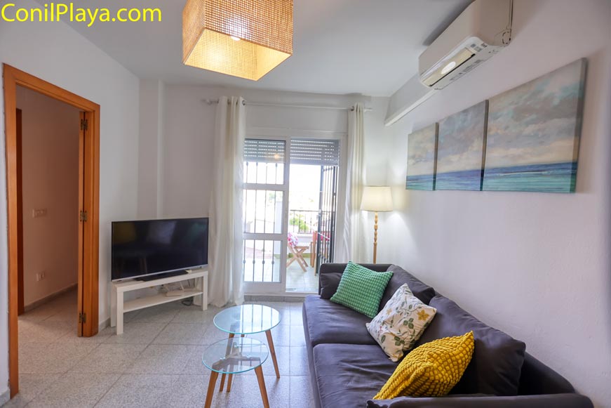Salón con sofá, mesa de cristal y televisión junto a ventanal