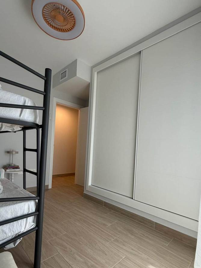 Dormitorio con ventilador de techo con luz, litera negra y gran armario empotrado con puertas correderas.