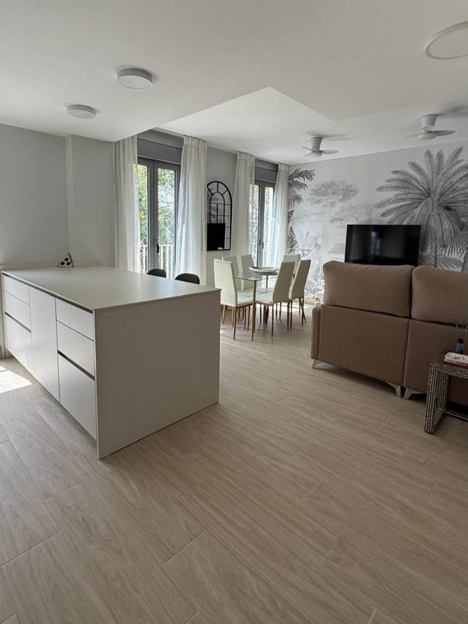 Isla de la cocina y comedor con mesa de cristal, sillas blancas y ventanales amplios