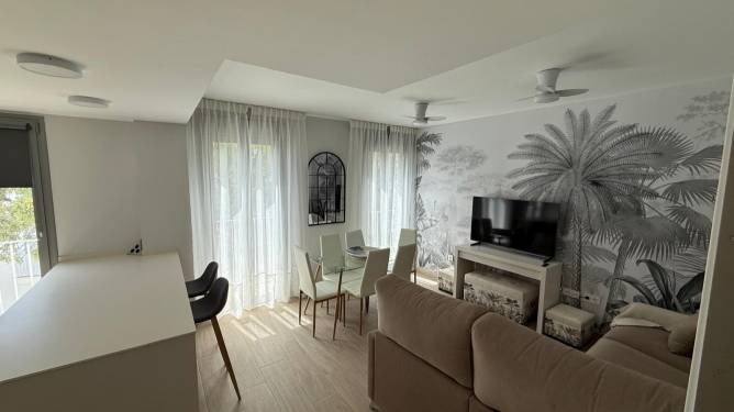 Vista general del salón moderno con sofá beige, mesa de cristal y mural decorativo en la pared