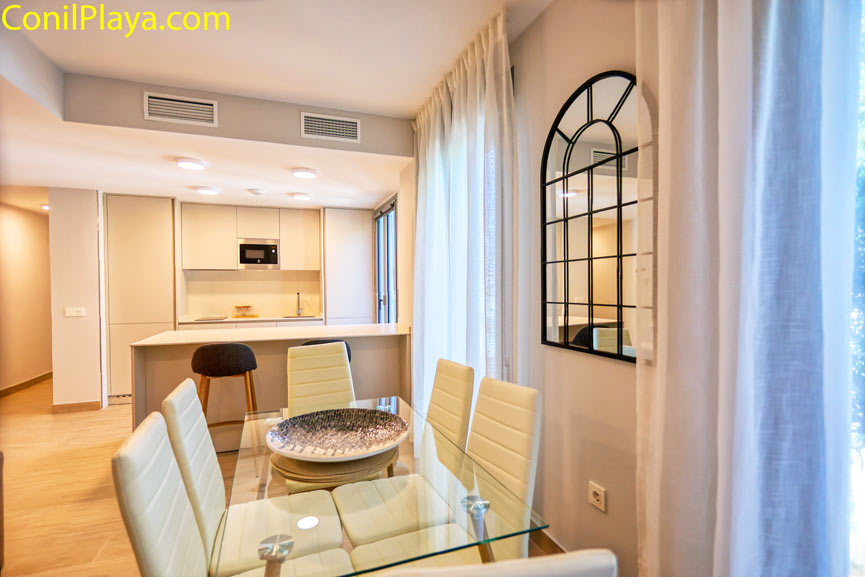 Comedor con mesa de cristal junto a cocina moderna abierta al fondo