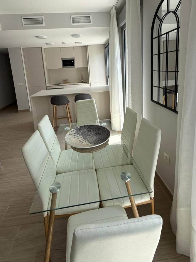 Comedor moderno con mesa de cristal y sillas blancas junto a cocina abierta