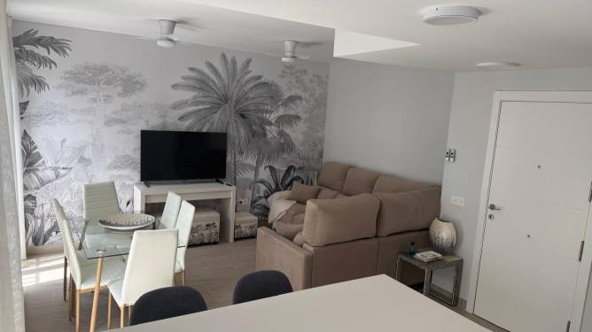 Salón moderno con sofá grande, televisor y mesa de comedor desde la cocina
