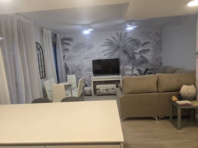 Salón con sofá beige televisor mural decorativo y mesa de comedor