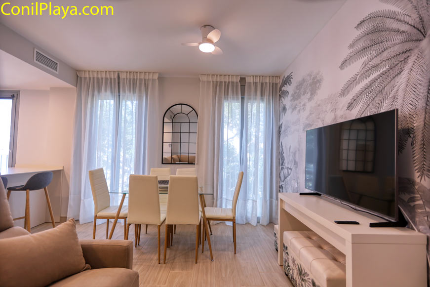 Comedor moderno con mesa de cristal y televisión vistos desde el salón