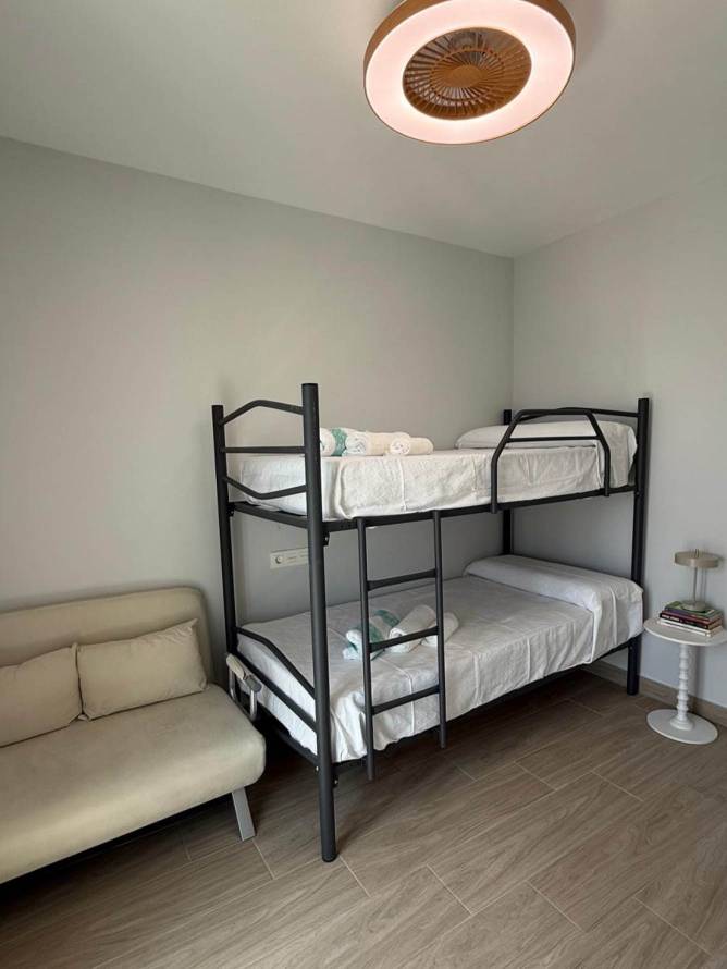 Literas negras en dormitorio con ventilador de techo con luz, cama supletoria plegada y mesita circular blanca