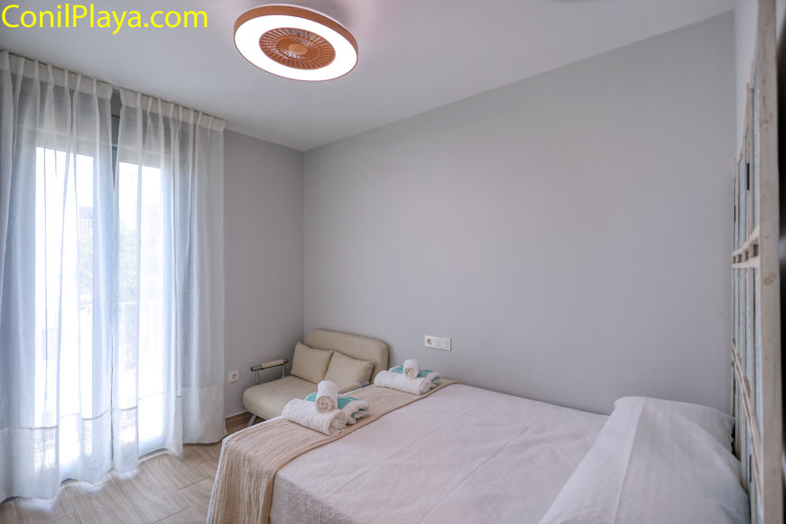 Dormitorio con cama de matrimonio y sofá junto a ventana grande