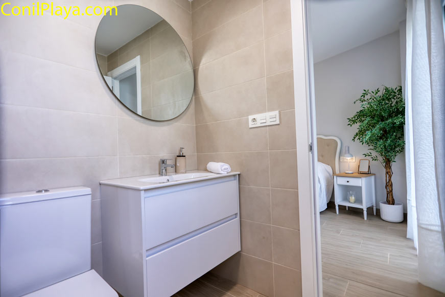 Lavabo y espejo redondo en baño junto a dormitorio moderno
