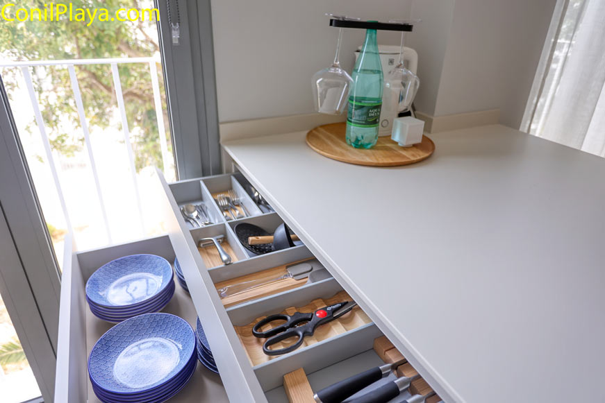 Vista de cajón abierto con cubertería y platos junto a ventana en cocina moderna