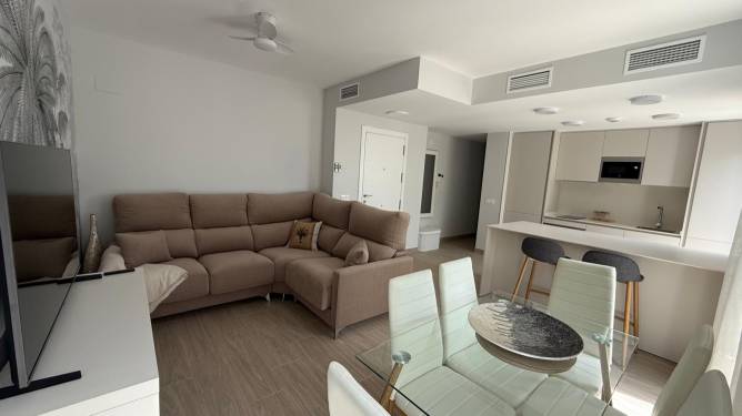 Salón con sofá en esquina y cocina americana y rejilla del aire acondicionado centralizado