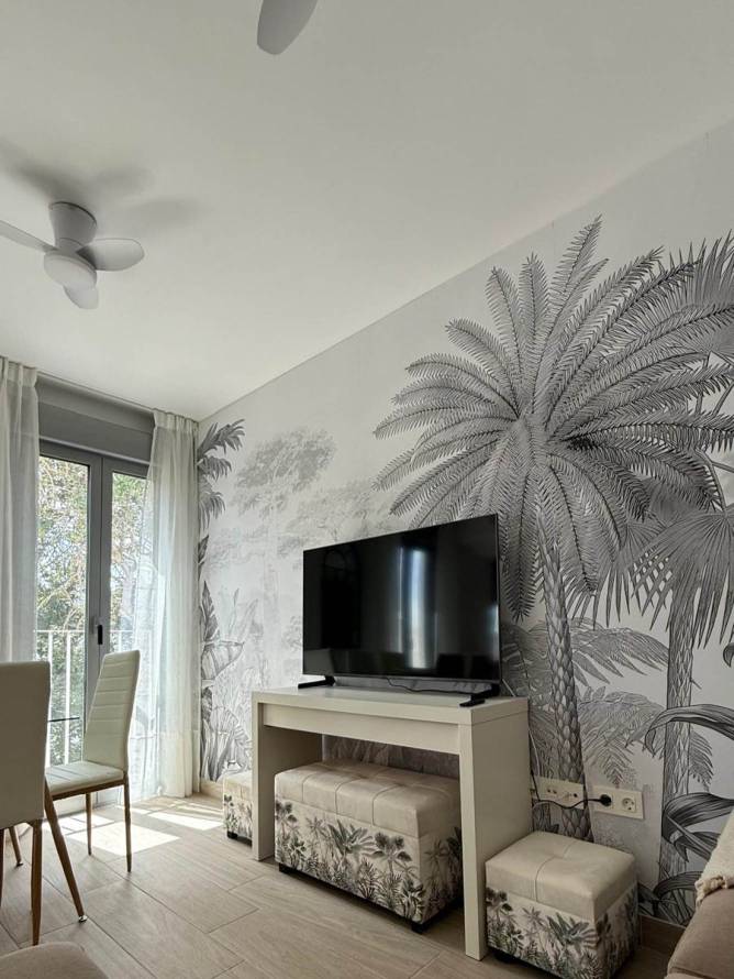 Salón con televisor sobre mesa y mural de palmeras decorativo