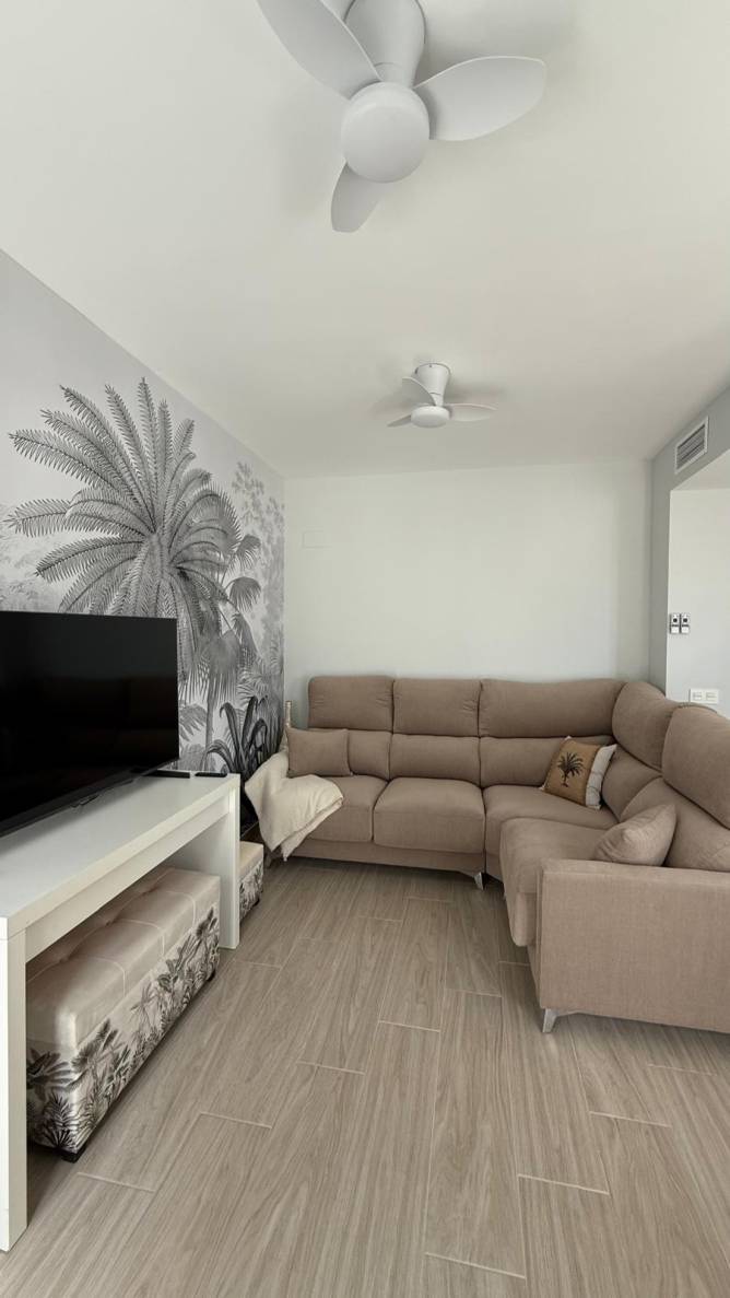 Salón moderno con sofá esquinero, ventiladores de techo y mural decorativo
