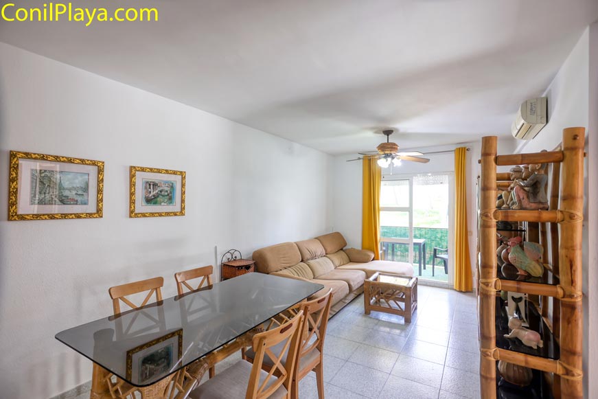 Comedor y salón. Perspectiva de la mesa del comedor con sillas y la zona de descanso al fondo.