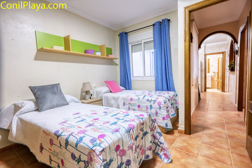 Habitación doble con camas individuales, estantería verde y vista al pasillo