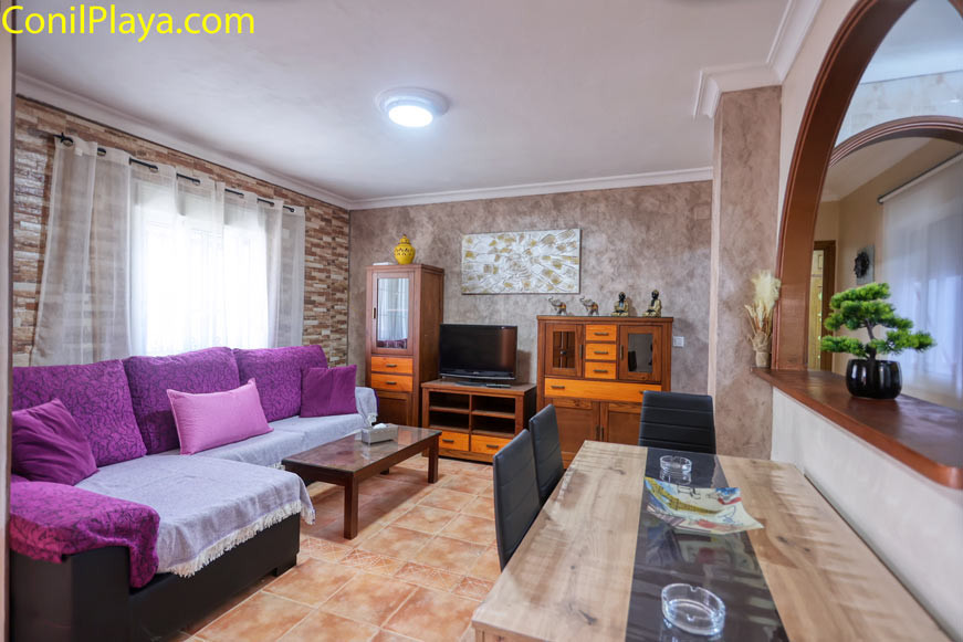 Sofa chaiselongue color púrpura en salón con pared de piedra