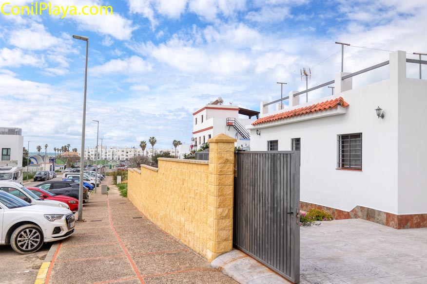Casa blanca con muro amarillo, portón metálico y coches aparcados en la calle bajo cielo nublado.