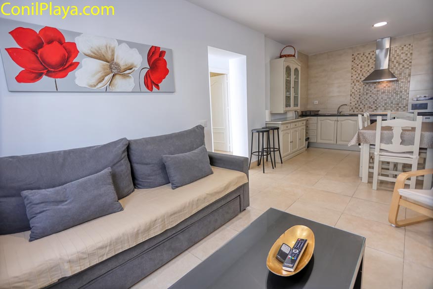 Salón con sofá gris, cocina integrada y mesa comedor, decoración moderna y luminosa.