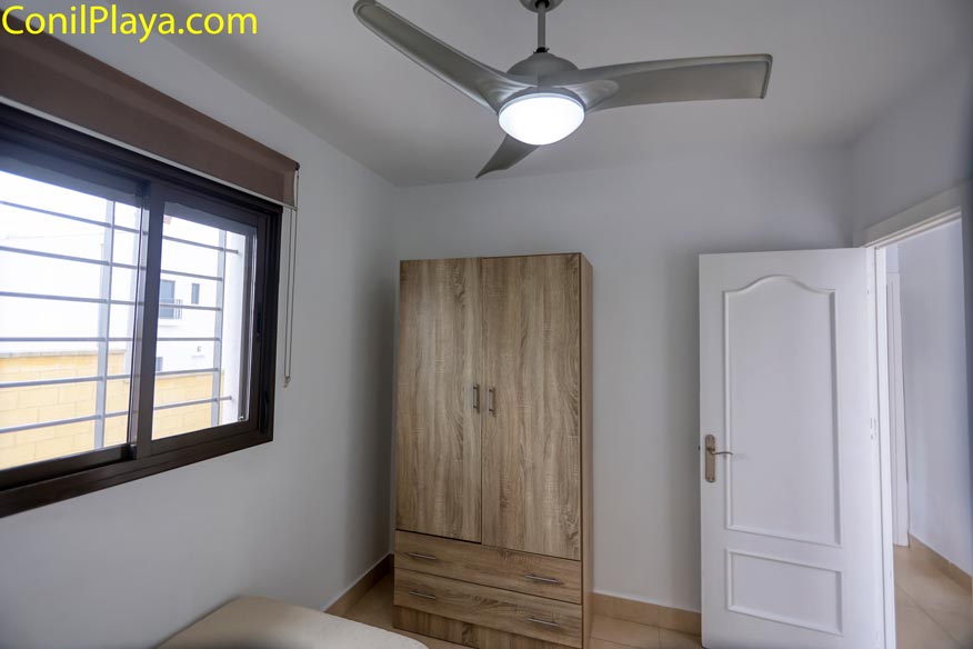 Armario de madera en dormitorio con ventilador de techo y puerta blanca.