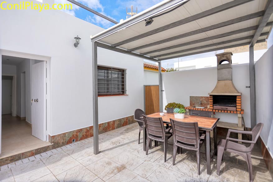 Patio con mesa, sillas de jardín, barbacoa techada y plantas decorativas