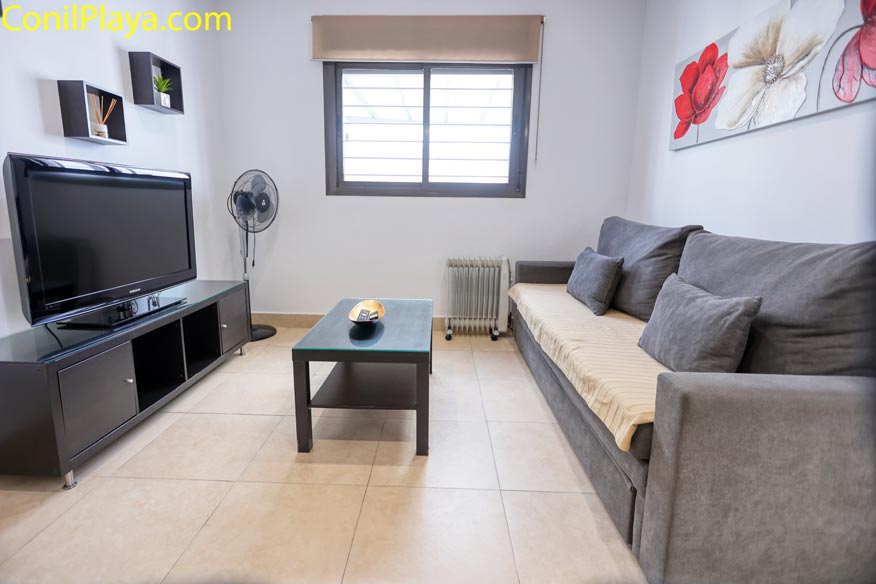 Salón moderno en Casa Mireva con sofá gris, TV y mueble, alquiler Conil con aparcamiento