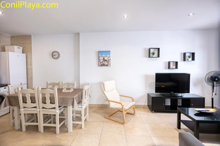 Espacio abierto que combina zona de comedor con mesa de madera y salón con TV.