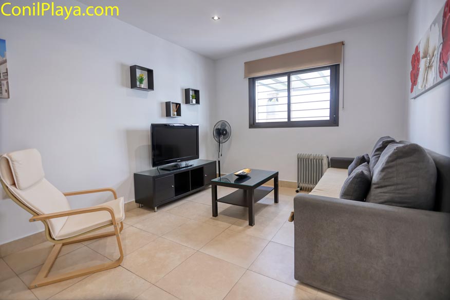 Salón con televisión de pantalla plana, sillón de madera y sofá gris.