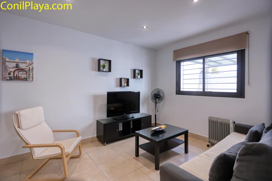 Salón con sofá, silla, televisor, ventana grande y decoración minimalista moderna.