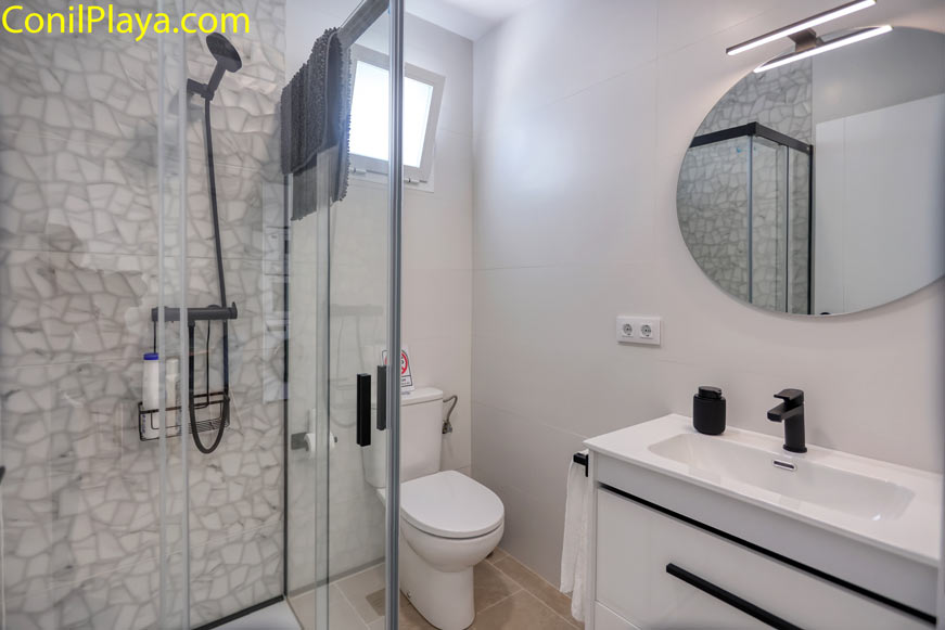 Baño moderno con plato de ducha de piedra, espejo circular y grifería negra