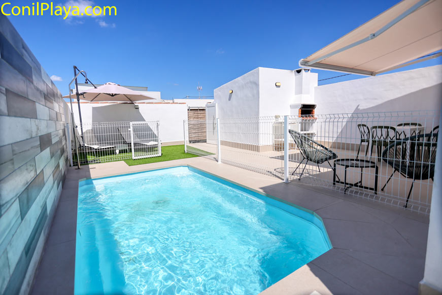 Vista general del patio privado con piscina, barbacoa de obra y comedor