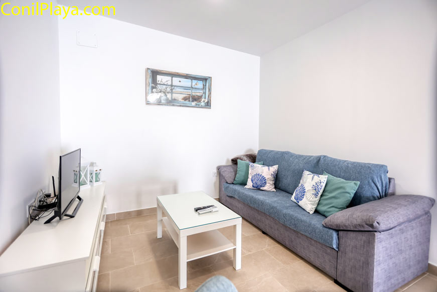 Sofá de tres plazas con cojines decorativos, mesita y televisión