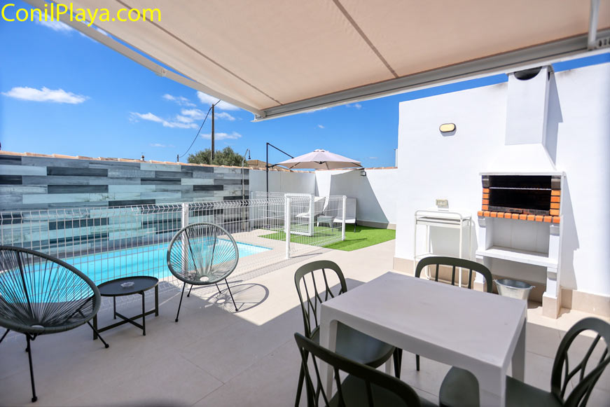 Zona exterior con piscina vallada, barbacoa de obra y comedor bajo toldo