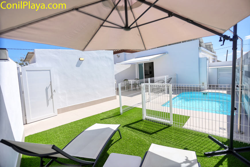 Terraza con césped artificial, tumbonas y sombrilla junto a la piscina