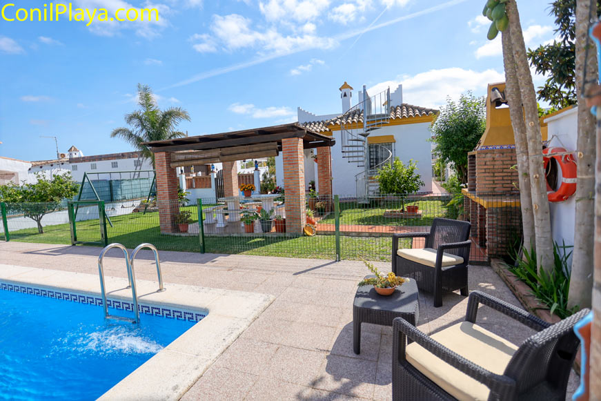 Piscina junto a zona con sillones, barbacoa y jardín en alojamiento vacacional