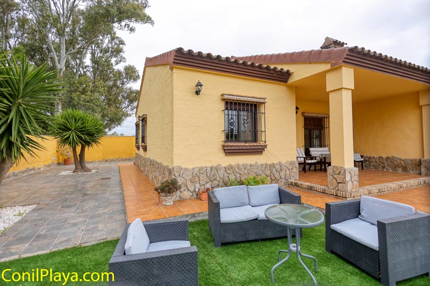 Vista lateral del alojamiento con terraza, muebles de exterior y jardín con plantas decorativas.