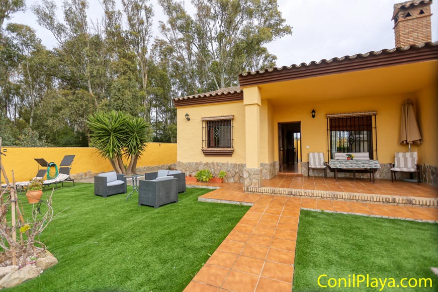 Alojamiento rural con porche, jardín de césped artificial y muebles de exterior.
