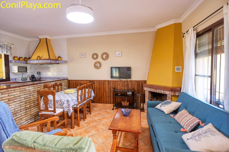 Salón acogedor con chimenea, sofá azul, mesa de comedor y cocina americana.