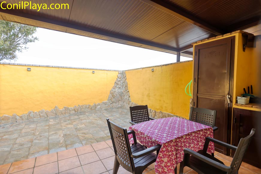Porche trasero cubierto con mesa, sillas y pared amarilla en chalet en alquiler en Conil