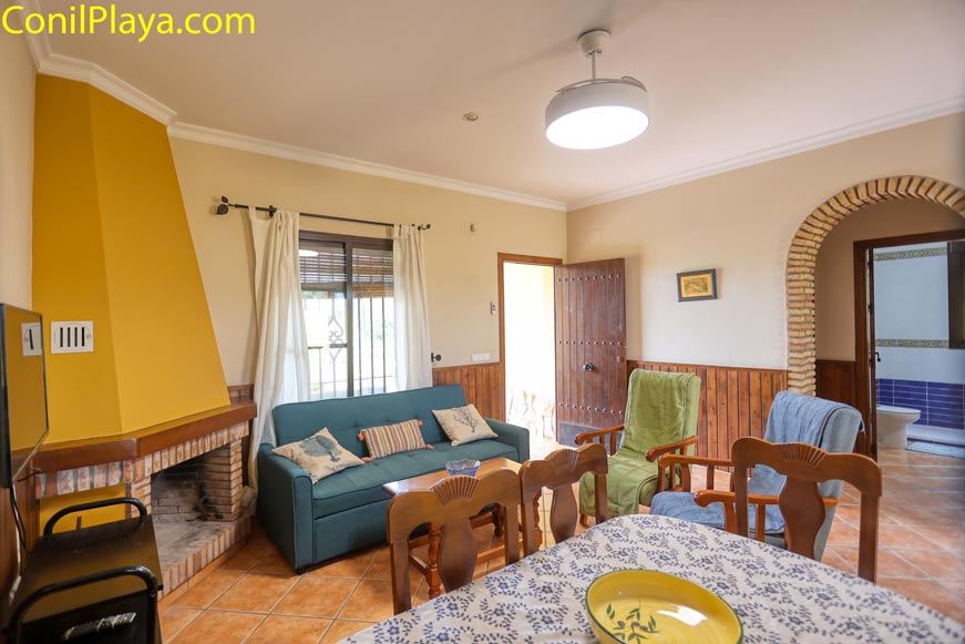 Salón con chimenea, sofá, sillones, mesa comedor y entrada de luz natural.