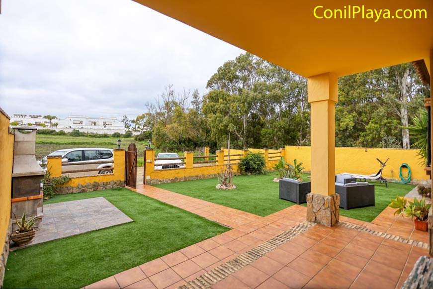 Jardín con césped artificial, barbacoa, muebles de exterior y plantas, rodeado de muro amarillo.