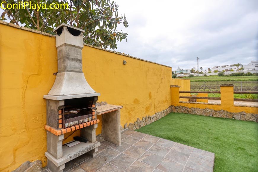 Jardín privado con barbacoa de obra y césped junto a muro amarillo