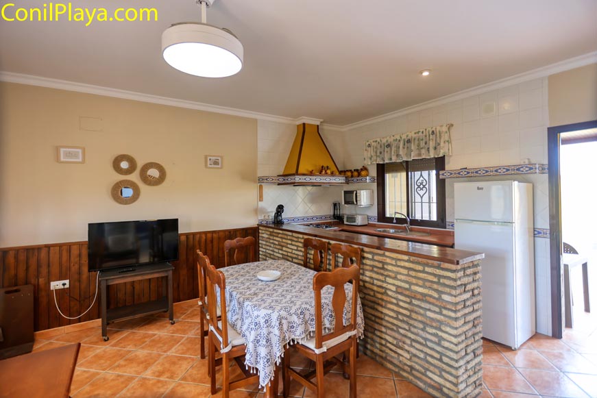 Comedor acogedor con mesa de madera, televisión y cocina americana equipada
