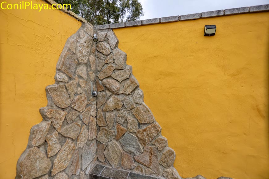 Ducha exterior de piedra junto a muro amarillo en zona de piscina