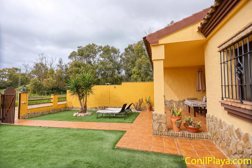 Jardín privado con césped artificial, árboles y tumbonas junto a casa amarilla