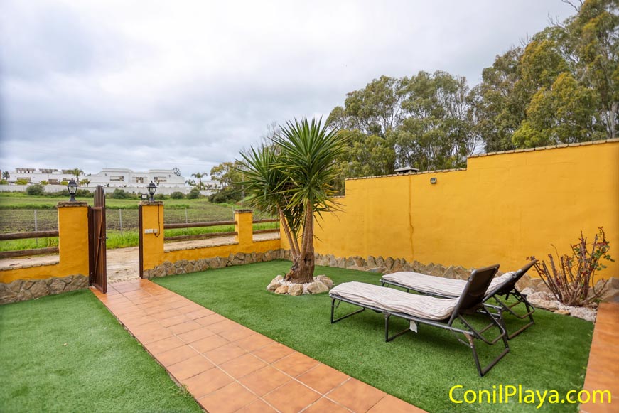 Jardín privado con césped artificial y tumbonas junto a muro amarillo