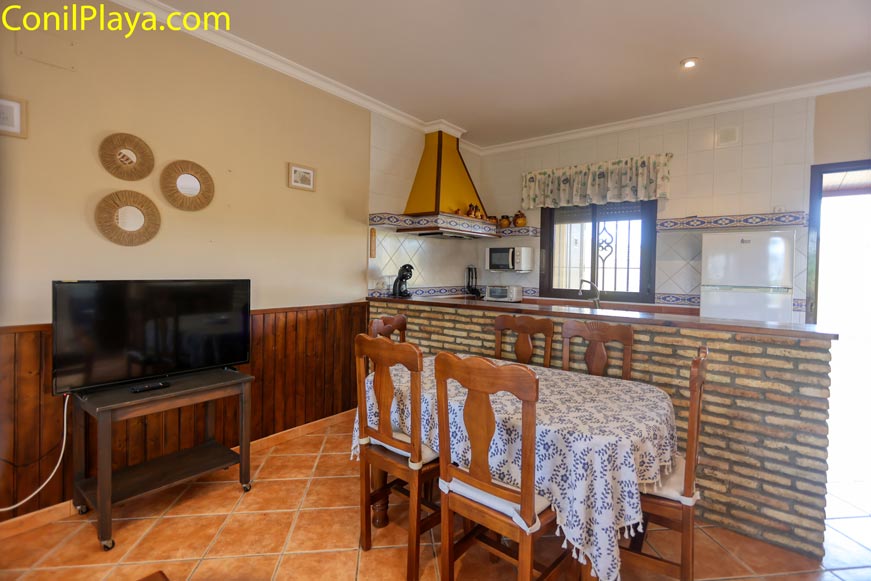 Salón luminoso con comedor, televisión y cocina abierta con barra de ladrillo