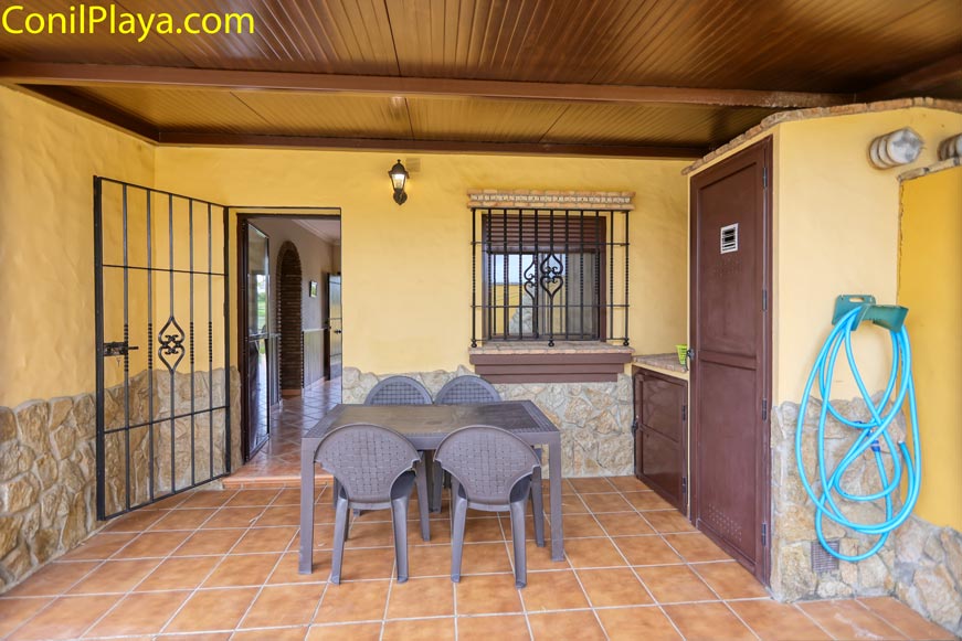 Porche cubierto con mesa y sillas de exterior frente a vivienda de fachada amarilla
