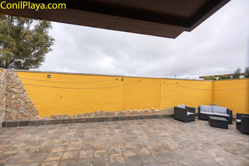 Terraza amplia con sofás grises y muro amarillo decorativo exterior