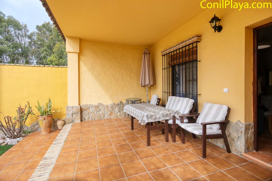 Porche cubierto con mesa y sillas junto a jardín y pared amarilla