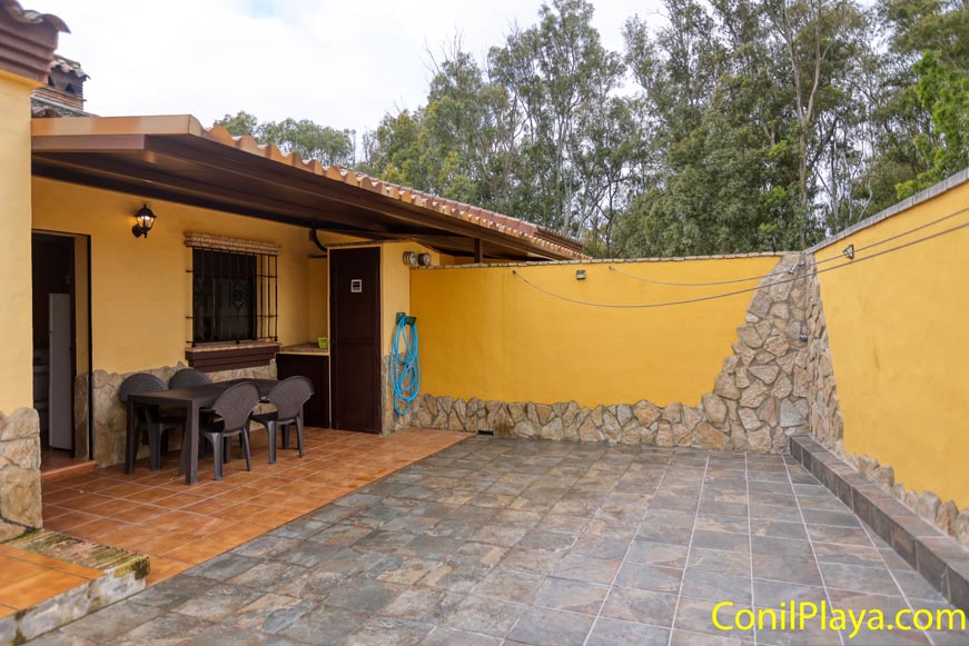 Porche trasero cubierto con mesa y sillas junto a patio amurallado